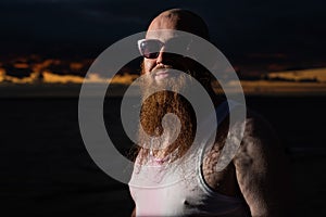 A humorous portrait of a brutal man in a T-shirt and boxers on the beach at sunset