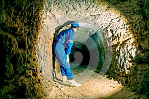Hunched worker in blue overall and safety helmet in underground tunnel. Dangerous employment.
