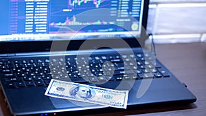 A hundred-dollar bill is placed on a laptop with a price chart for Forex, the market, stocks, bonds, or securities. Working place