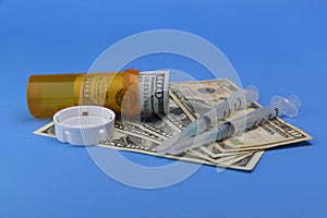 Hundred dollar bill and smaller dollar bills with a pill bottle and syringes representing the high cost of opiate addiction