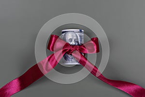 Hundred dollar bill tied with red bow on grey background. Money, gift wrapped in red bow and ribbon, US currency, cash, business