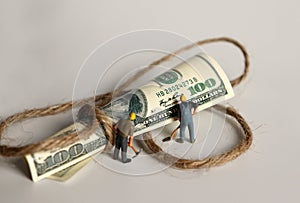 A hundred-dollar bill tied to a rope and miniature people.