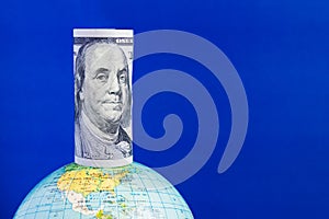 A hundred-dollar bill on top of the globe on a blue background