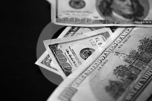 Hundred dollar bills on a dark background, black and white