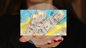 Hundred dollar bills fall on the flag of Ukraine, and the girl holds the video with her hand