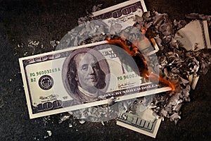 A hundred dollars burn in a fire on a black background, the concept of burning money, inflation, the cost of money