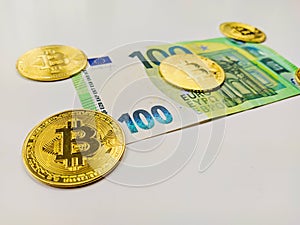A hundred euros trapped under golden bitcoin coins representing the emergence of cryptocurrencies and fall of paper money