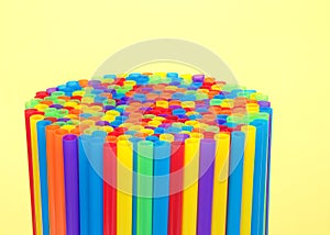 Hundreds of colorful plastic straws upright on yellow background