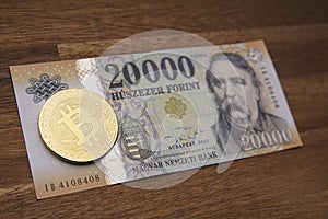 Hungarian forint 20 000 forint banknote Ferenc DeÃ¡k. Brown wooden table. Next to it is a gold bitcoin digital cryptocurrency coin