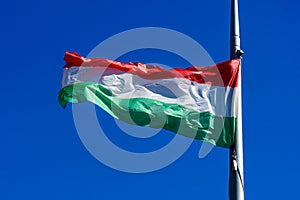 Hungarian national flag blowing in the wind in direct sunlight towards clear blue sky in a sunny day