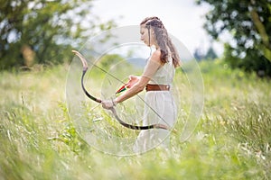 A Hungarian woman in a linen dress standing with a bow in the tall grass