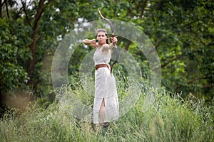 A Hungarian woman in a linen dress standing with a bow in the tall grass