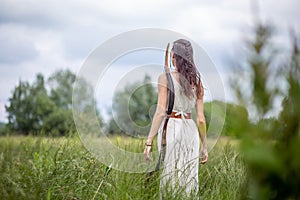 A Hungarian woman in a linen dress standing with a bow in the tall grass