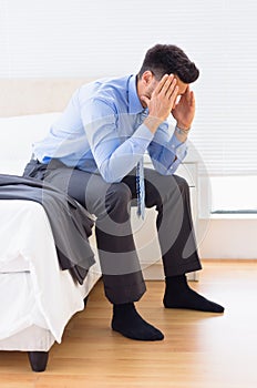 Hungover businessman sitting at edge of bed