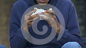 Hungry african-american young male greedily eating sandwich outdoor, poverty