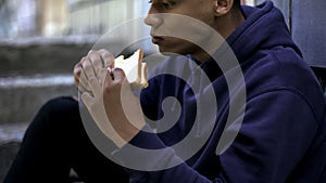 Hungry afro-american teenager eagerly eating sandwich, poor family, crisis