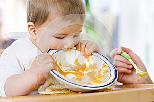 Hungry baby boy eating food next to his mother.