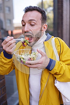 Hungry bearded man eating fresh salad during walk