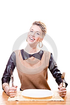 Hungry beautiful blond woman smiling holding cutlery in her hand with empty plate in front of her happy smiling