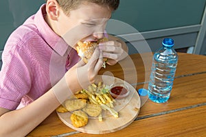 Hungry boy eagerly bites a burger during lunch in a fast food cafe