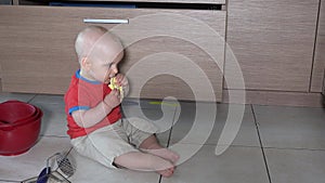 Hungry boy eat food sitting in mess on kitchen floor