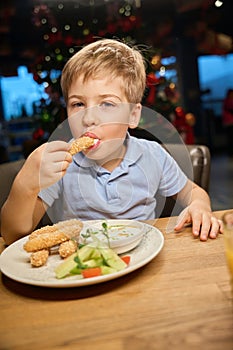 Hungry boy eating nuggets in cafe during New Years Eve celebration