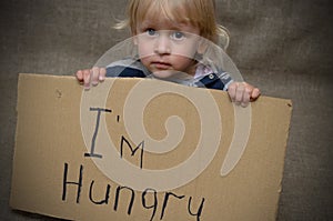 A hungry boy and a girl with a cardboard tablet with the inscription I`m hungry . The social problem.