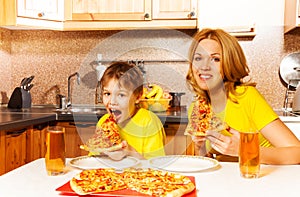 Hungry boy and his mother eating pizza in kitchen