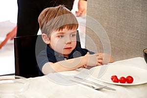 Hungry child sitting in chair at table in kitchen and waiting for meal and lunch. Boy is curious what he will get for meal.