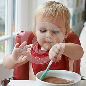 Hungry, cute and baby eating porridge for health, nutrition or child development at home. Food, sweet and girl toddler