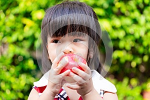 Hungry cute girl eats a red apple. Headshot of Asian children gnaw fruit. Child held it with both hands so that she could bite.