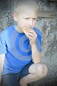 A hungry dirty boy greedily eats a crust of bread against the wall. Toning.