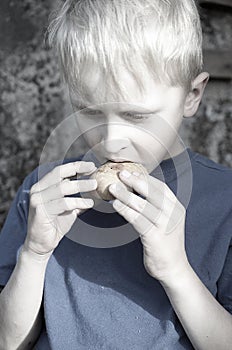 A hungry dirty boy greedily eats a crust of bread against the wall. Toning.