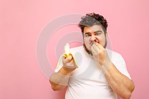 A hungry fat guy on a diet eagerly eats a banana and looks into the camera with an emotional face. Funny young overweight man