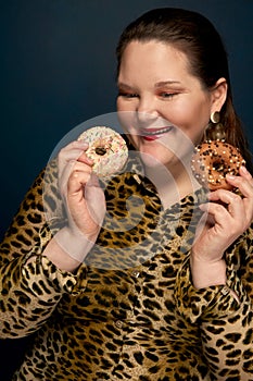 A hungry girl in a leopard blouse and looks at donuts. Dark blue background.