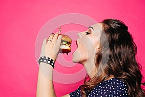 Hungry girl with opened mouth eating big hamburger.