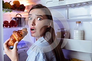 Hungry girl opening fridge, eating baking late in night