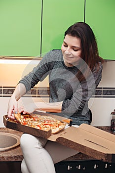 Hungry girl sitting on kitchen having dinner of italian pizza.