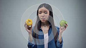 Hungry girl trying to choose between donut and apple, healthy eating, temptation
