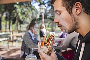 Hungry guy is enthusiastically looking at his burger. He is sitting at the restauraunt terrace