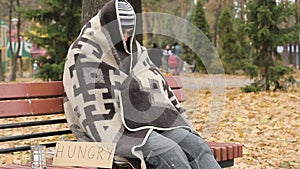 Hungry homeless frozen man sitting on bench and trying to get warm, poverty