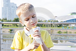 Hungry kid eating street food on the beach in summer. A little emotional boy eating fried sausages on a stick