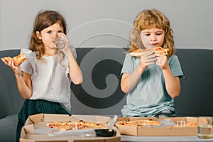 Hungry kids eating pizza. Two young children bite pizza indoors.
