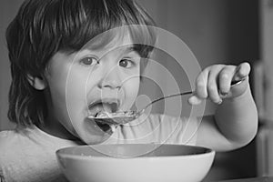Hungry little boy eating. Cheerful baby child eats food itself with spoon. Tasty kids breakfast. Baby eating food on