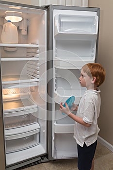 Hungry little boy looking into empty fridge photo