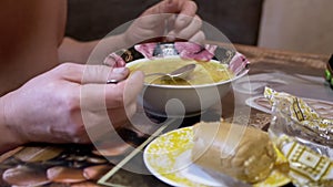 Hungry Male after Working Day Eats Soup in Home Kitchen, Watches Video on Mobile Phone