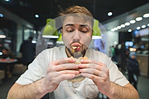 Hungry man with a beard greedily eats a burger. A funny man looking at a sandwich. Focus on the burger
