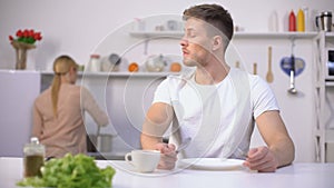 Hungry man eagerly waiting for dinner, wife cooking on background, starvation