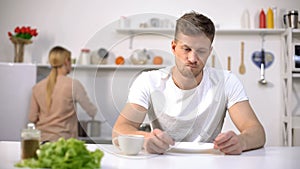 Hungry man eagerly waiting for dinner, wife cooking on background, starvation photo