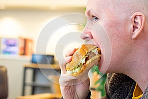 Hungry man eating or gobbling up a hamburger